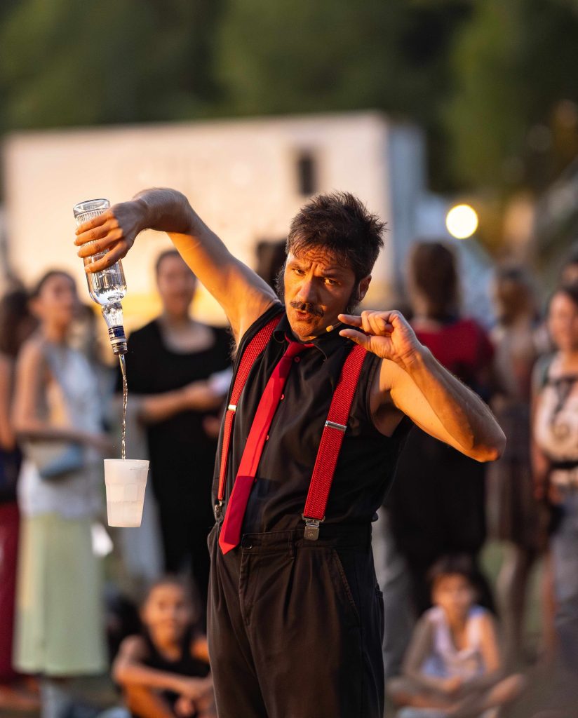 Piero Ricciardi, in arte Pier La Truf Artista di strada durante un'esibizione di mixology o teatro fisico in un evento serale. Atmosfera calda con luci outdoor e pubblico coinvolto.